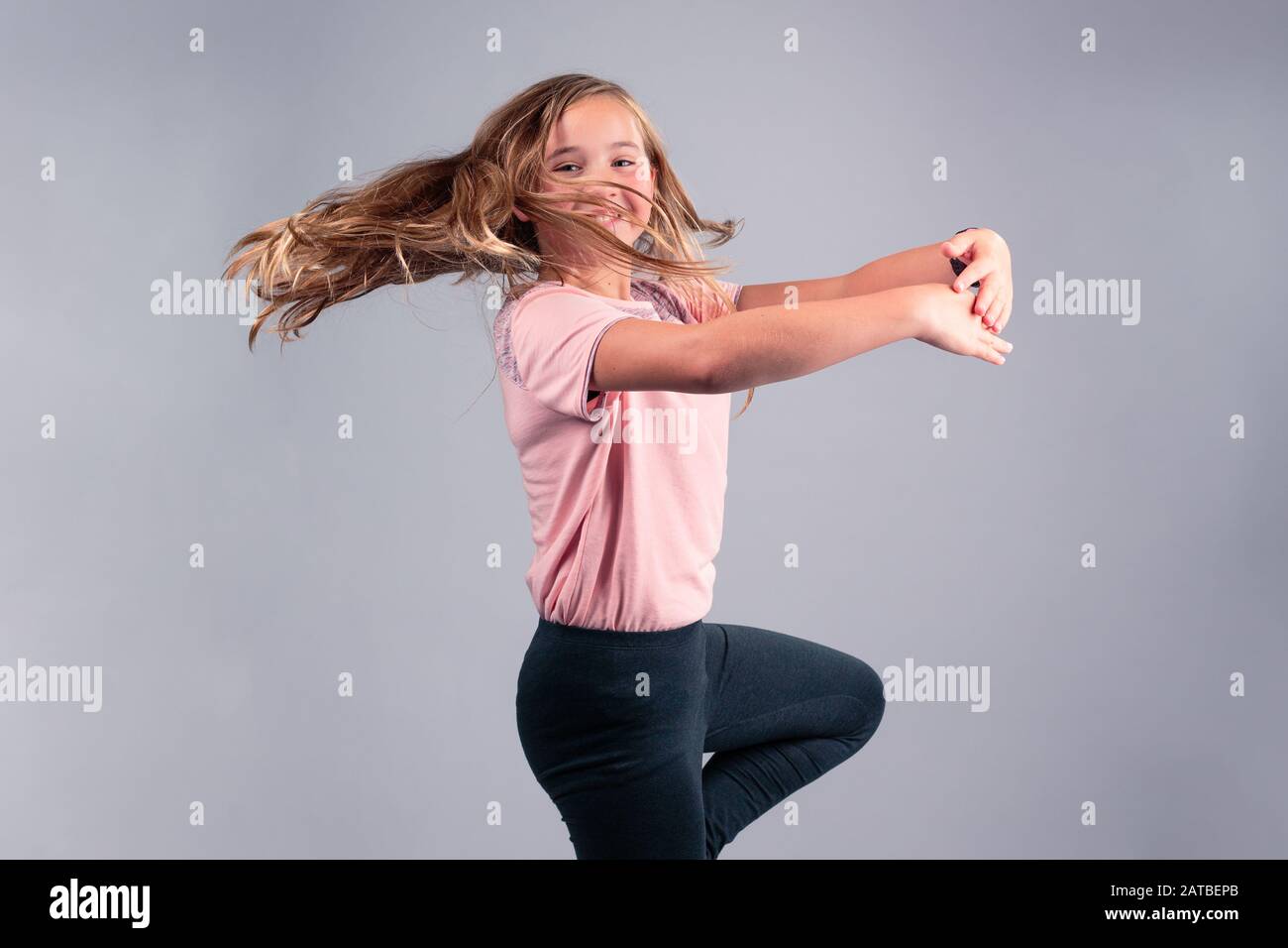 Gaie de 11 ans fille portant un t-shirt rose et un pantalon noir avec une  longue danse blonde. Isolée sur fond gris Photo Stock - Alamy