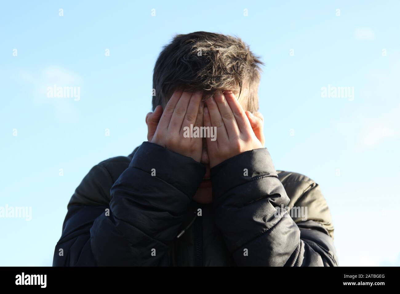 Un jeune garçon de 12 couvre son visage boueux avec ses mains, face à la caméra Banque D'Images