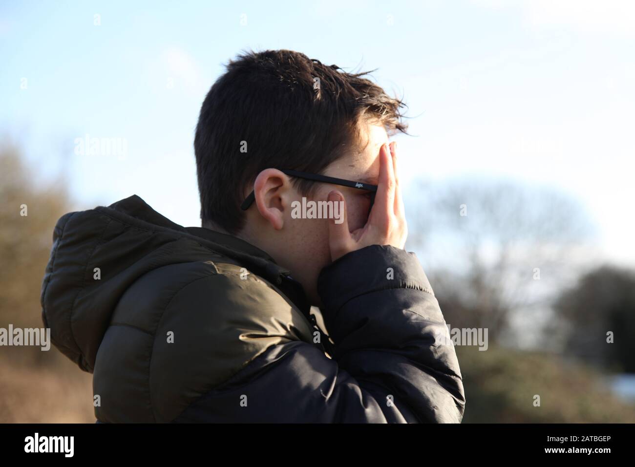 Un jeune garçon de 12 couvre son visage boueux avec ses mains, profil latéral Banque D'Images
