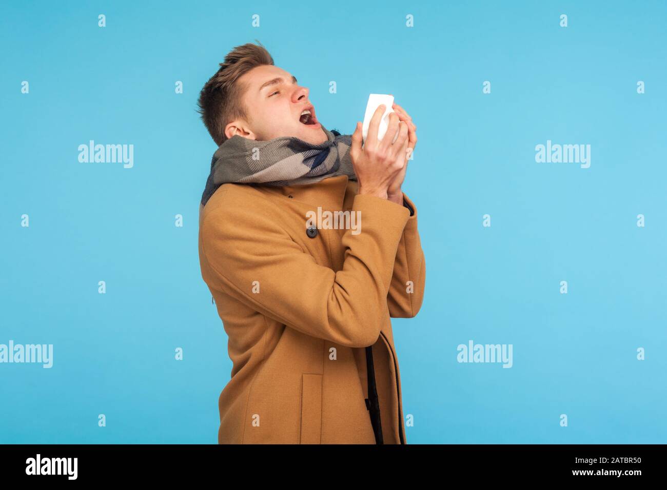 Saison grippale. Homme malade malsain de la grippe en automne manteau et écharpe éternuer fortement dans les tissus, se sentir mal avec le nez liquide, a attrapé froid ou allergie Banque D'Images