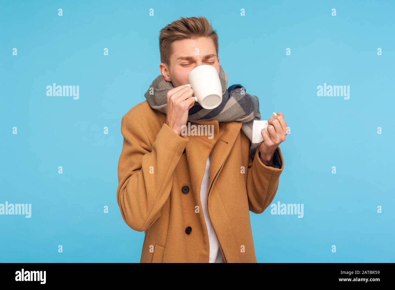 Traitement de la grippe et auto-soins. Homme malade en automne manteau et foulard buvant la médecine avec thé chaud, tenant des tissus pour le nez liquide, la fièvre souffrant, headach Banque D'Images