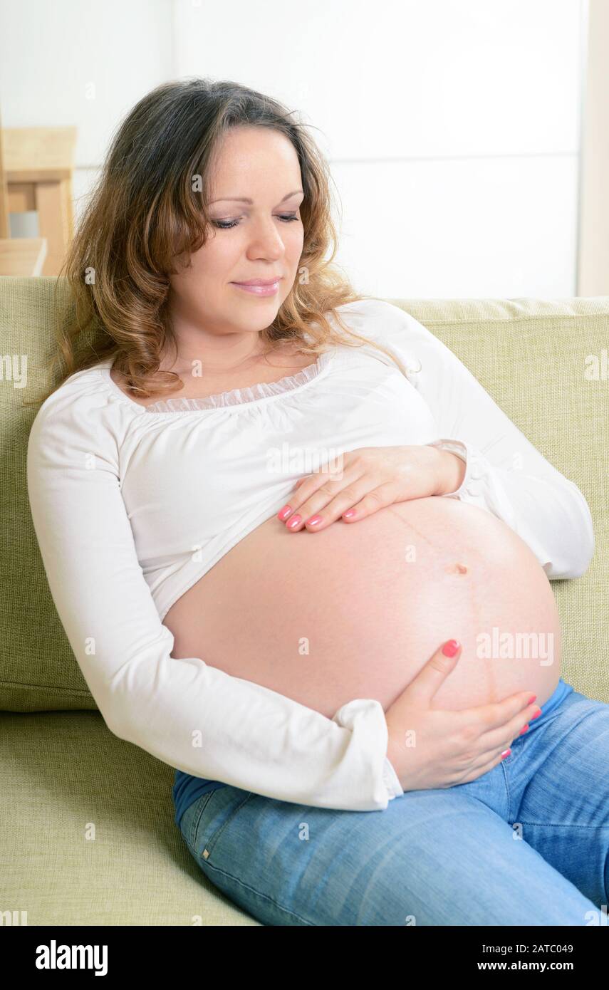 Bonne femme enceinte assise sur le canapé à la maison. Le neuvième mois de grossesse. Banque D'Images