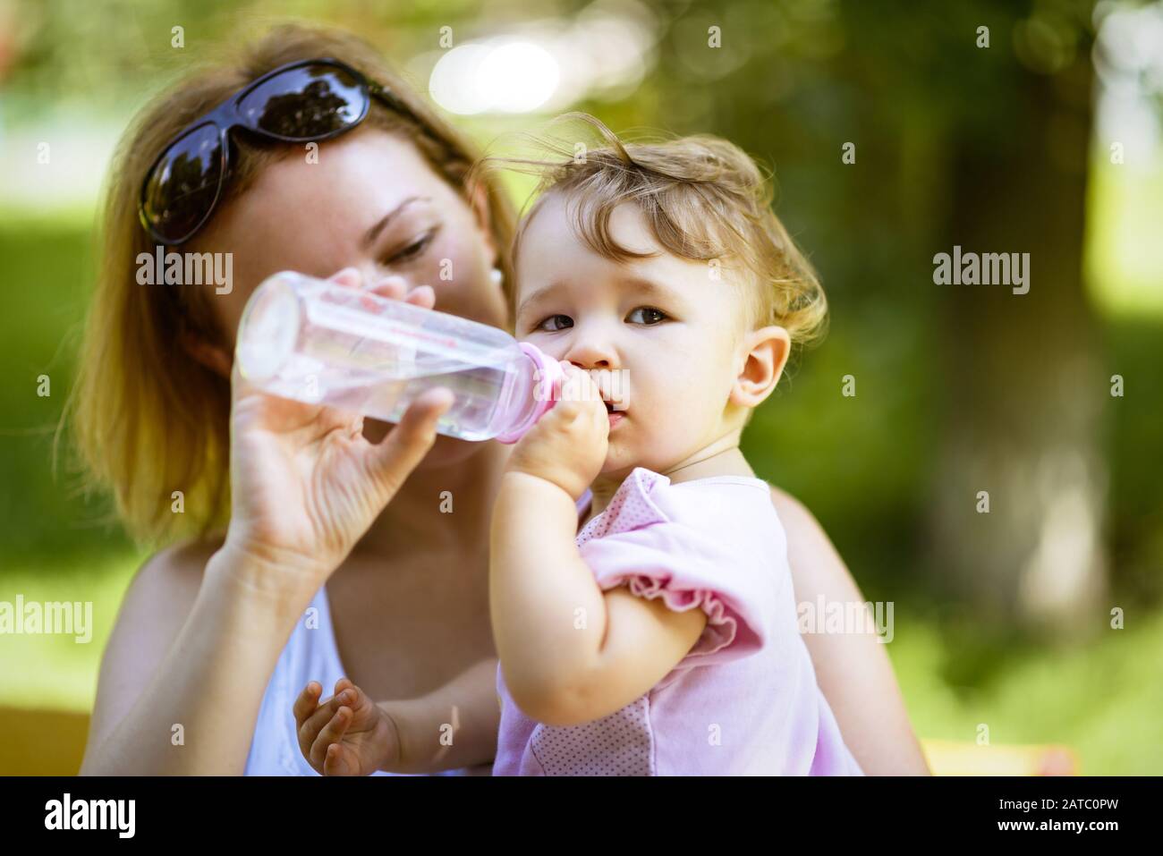 La mère donne à sa fille de bébé de boire de l'eau à partir d'une bouteille dans un parc. Enfant extérieur d'un an. Banque D'Images