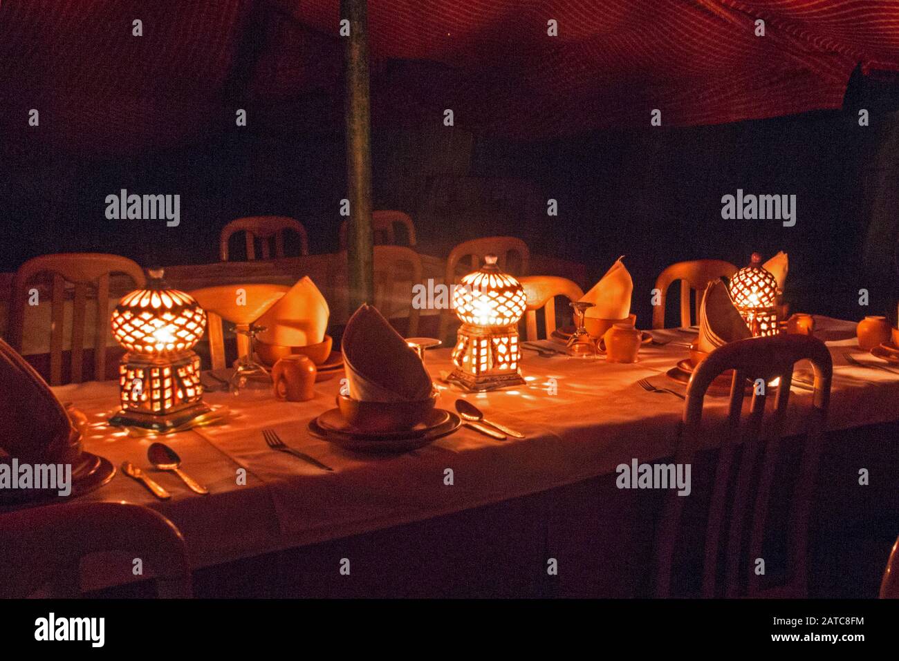 La table est couverte pour le dîner dans le restaurant du camp. La lumière provient de lampes de poterie traditionnelles tunisiennes à cage d'oiseaux. Banque D'Images