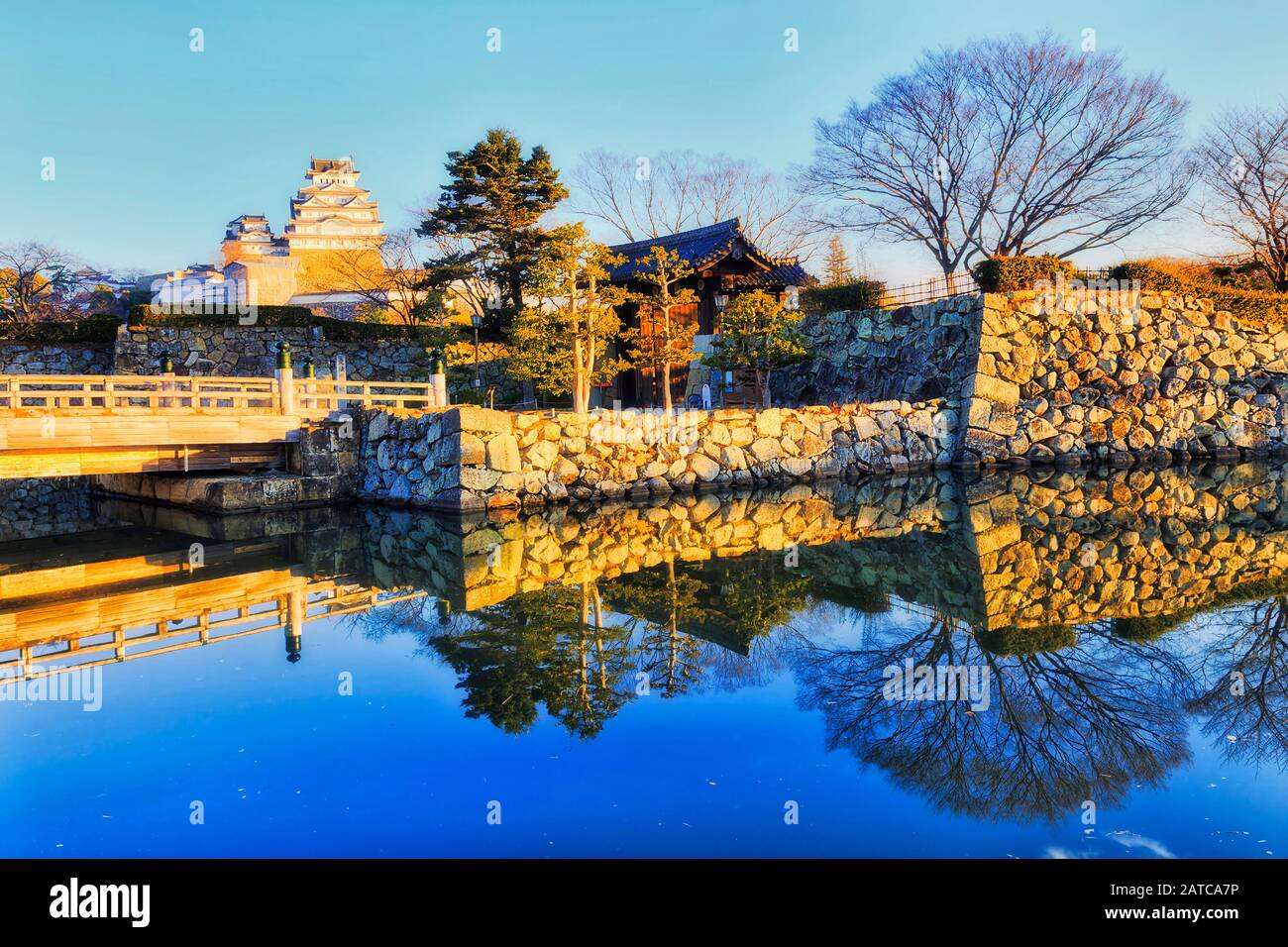 Pont en bois au-dessus de la moat remplie d'eau autour du château blanc près d'Osaka au Japon – Himeji-jo un matin ensoleillé. Banque D'Images