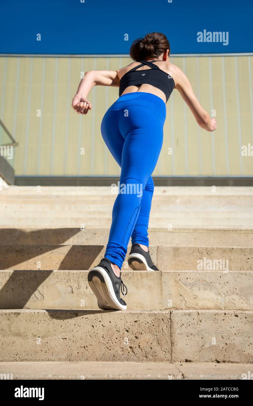 vue arrière d'une femme sportive qui court des marches en béton à l'extérieur, vêtements de sport bleus. Banque D'Images