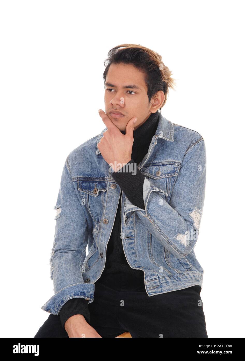 Un jeune homme léger assis dans une veste de Jean et un pantalon noir sur une chaise, reposant, isolé pour le fond blanc Banque D'Images