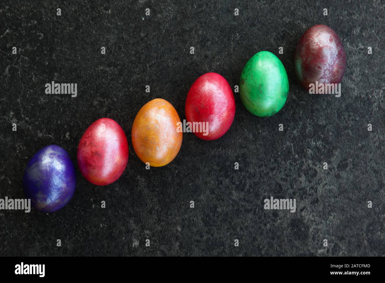 Six œufs colorés en diagonale sur la surface anthracite Banque D'Images