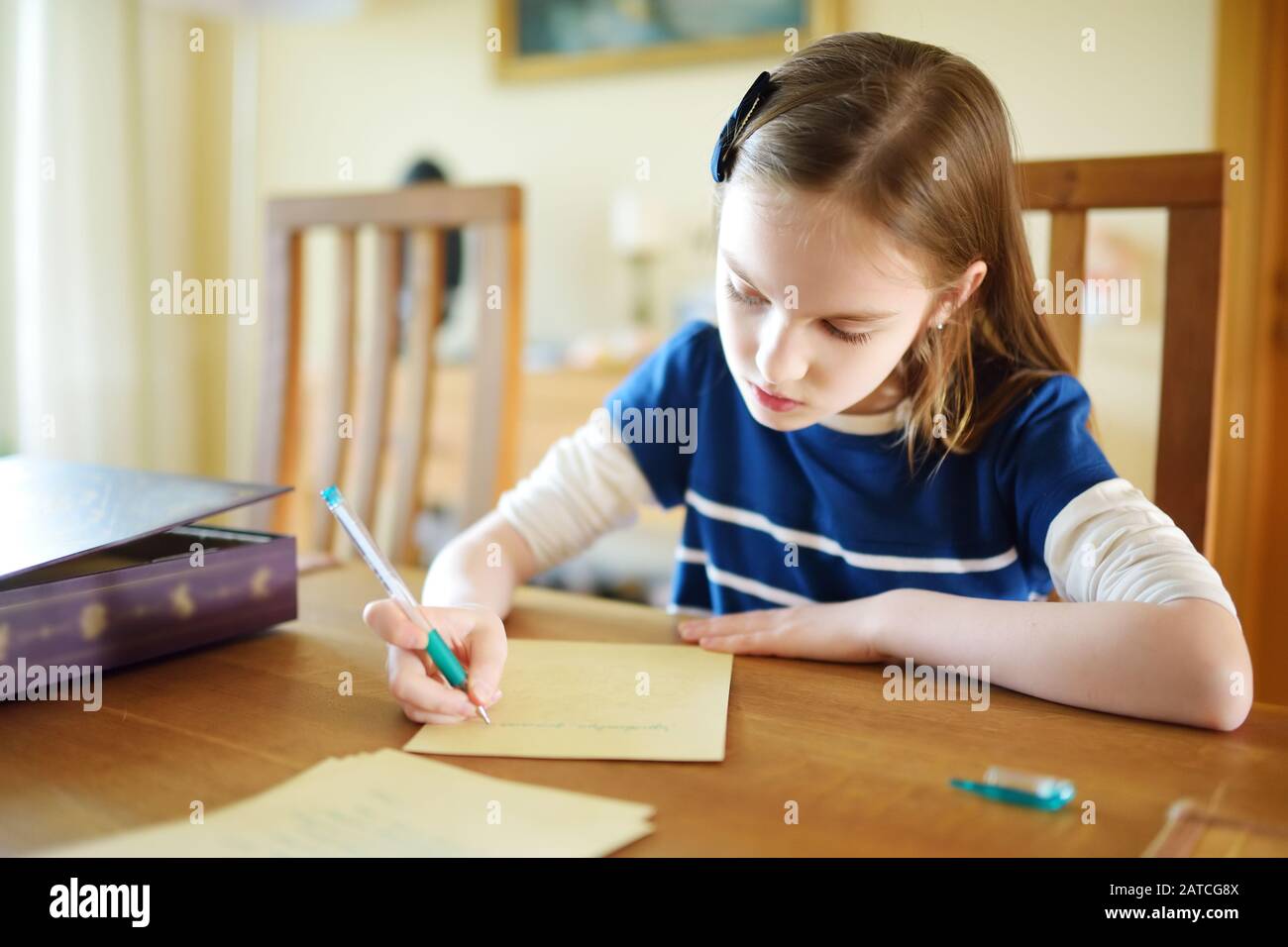 Une petite écolière intelligente qui fait ses devoirs à sa table à la maison. Apprentissage de l'enfant à écrire et à lire. Éducation et apprentissage pour les enfants. Banque D'Images