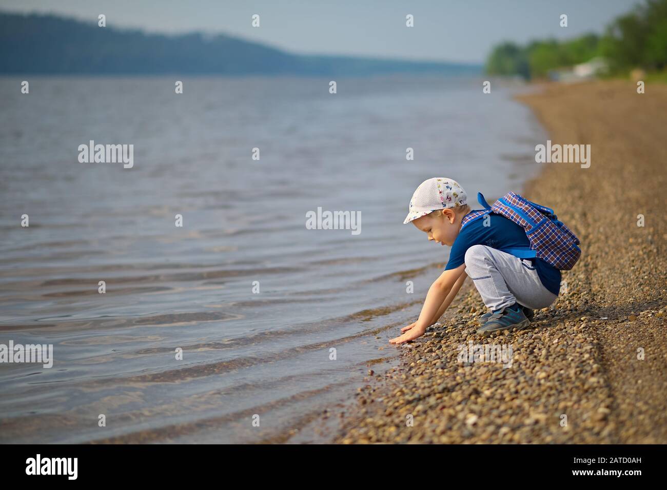 Un petit garçon touche l'eau avec ses mains dans une grande rivière. Banque D'Images