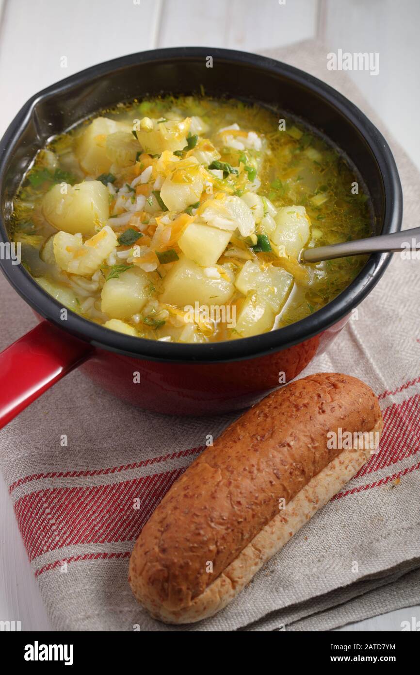 Soupe végétalienne avec pomme de terre, céleri, carotte, riz et oignon vert dans une casserole rouge Banque D'Images