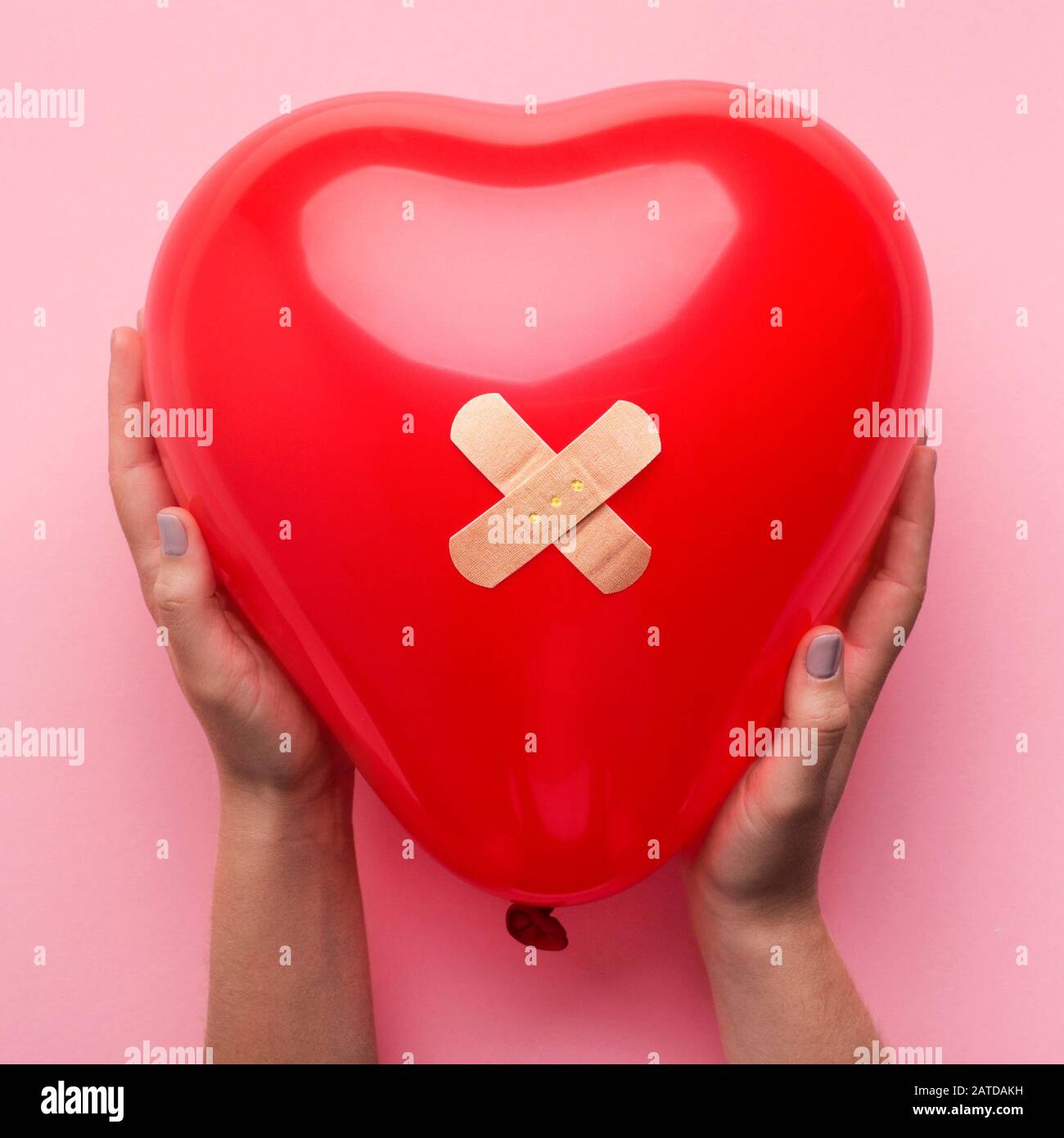 Femme tenant Le coeur Cassé avec bandage sur rose Banque D'Images
