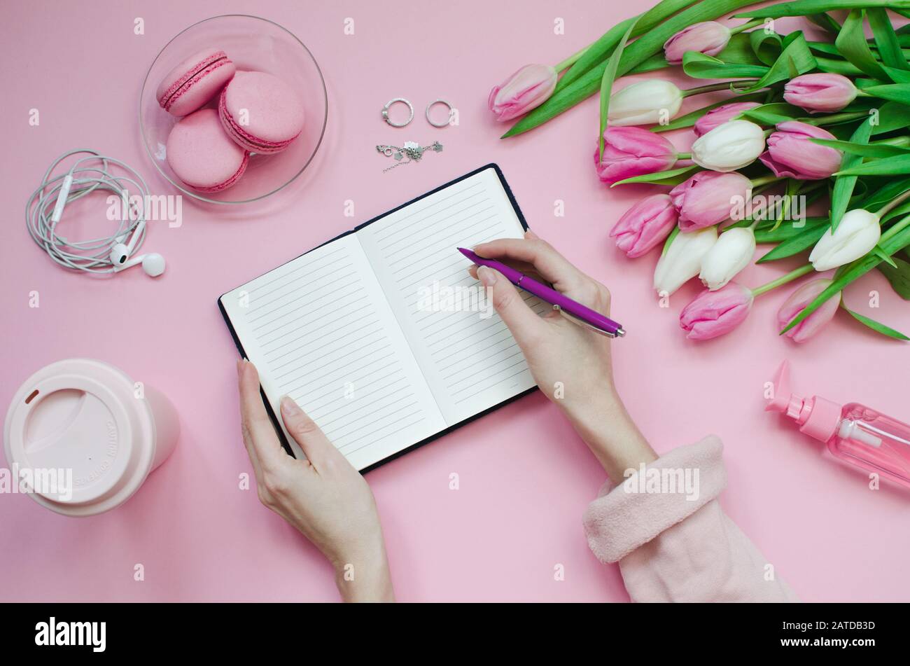 Fille écrivant la liste de souhaits pour les plans futurs. Composition plat de laïcs avec des fleurs, bloc-notes, une tasse de café et des bonbons Banque D'Images