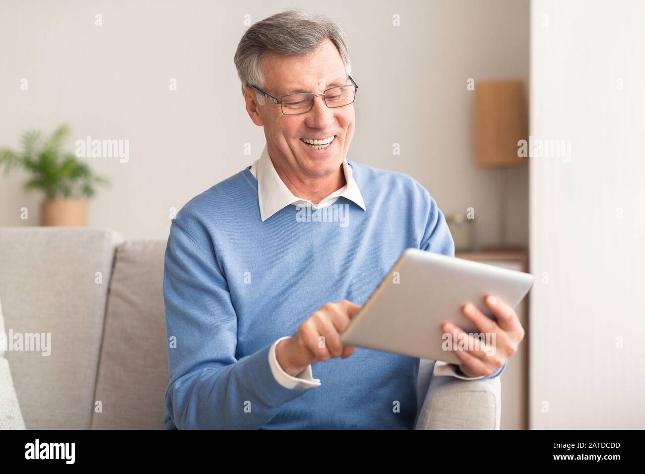 Homme Senior Avec Tablette Ordinateur Navigation Internet Assis Sur Canapé Banque D'Images