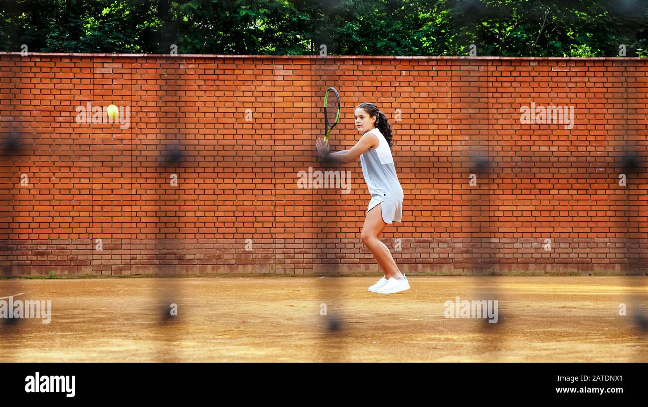 Jeune fille bloquant le ballon avec le raquette de tennis pendant l'entraînement. Grille floue au premier plan. Banque D'Images