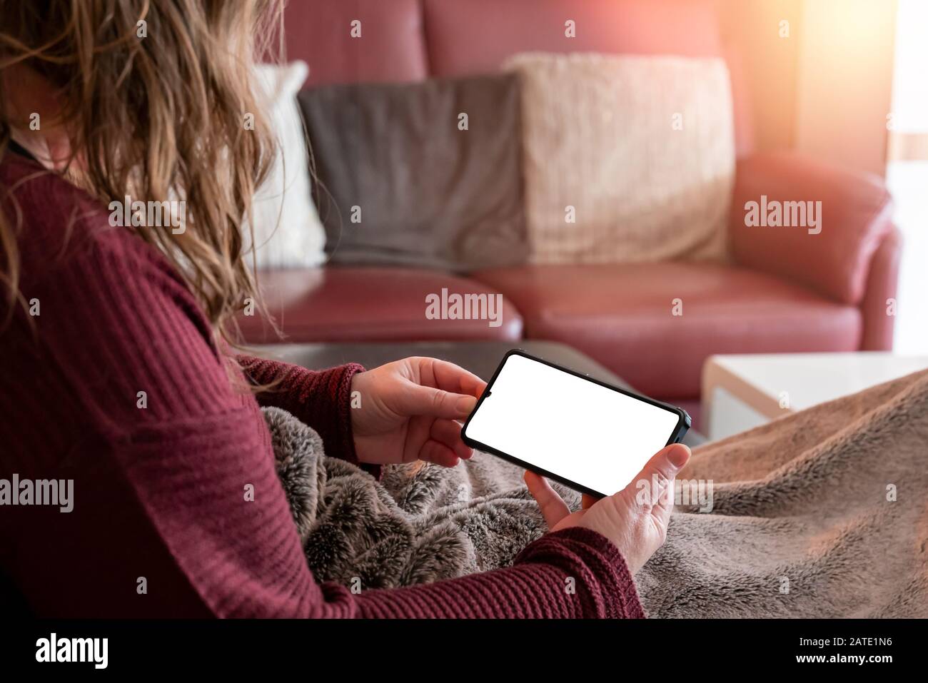 Une femme d'âge moyen est posée sur le canapé à la maison. Elle regarde le smartphone. Espace de copie pour vos propres conceptions. Ambiance rouge. Banque D'Images