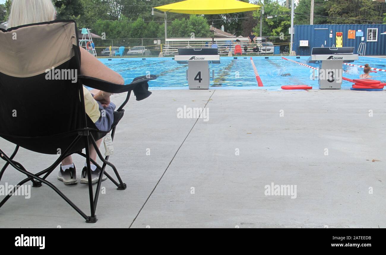 Femme avec chapeau assis sur une chaise noire regardant les nageurs dans la piscine Banque D'Images