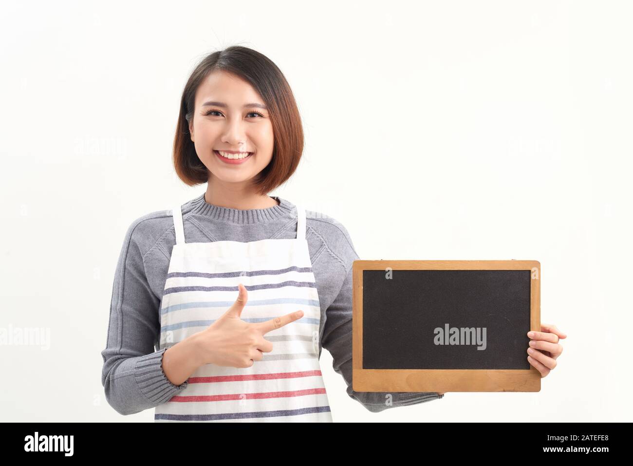 Serveuse asiatique pointant vers un tableau vide et regardant l'appareil photo tout en se tenant sur fond blanc Banque D'Images