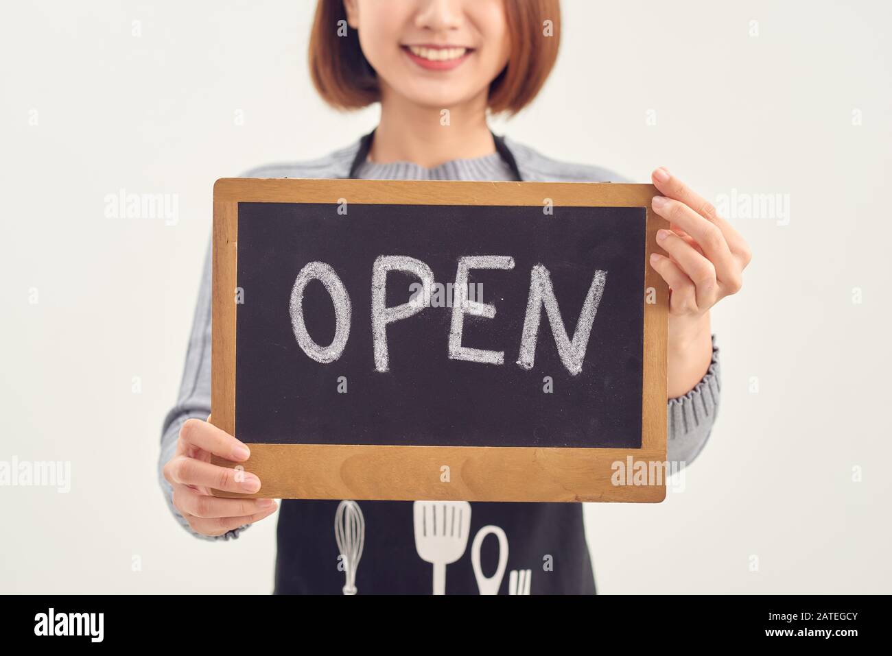 Il est ouvert ici. Une femme souriante tient un signe avec l'inscription "ouvert" sur un fond blanc isolé. Banque D'Images