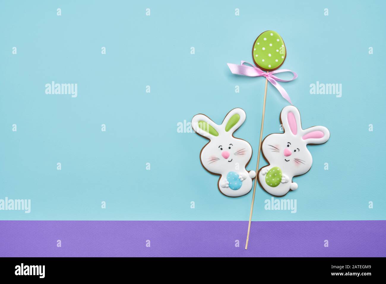 De la vue ci-dessus des cookies colorés au gingembre glacés isolés sur fond bleu et violet. Délicieuse pâtisserie maison en forme de lapins de pâques tenant des œufs. Concept de vacances, boulangerie. Banque D'Images