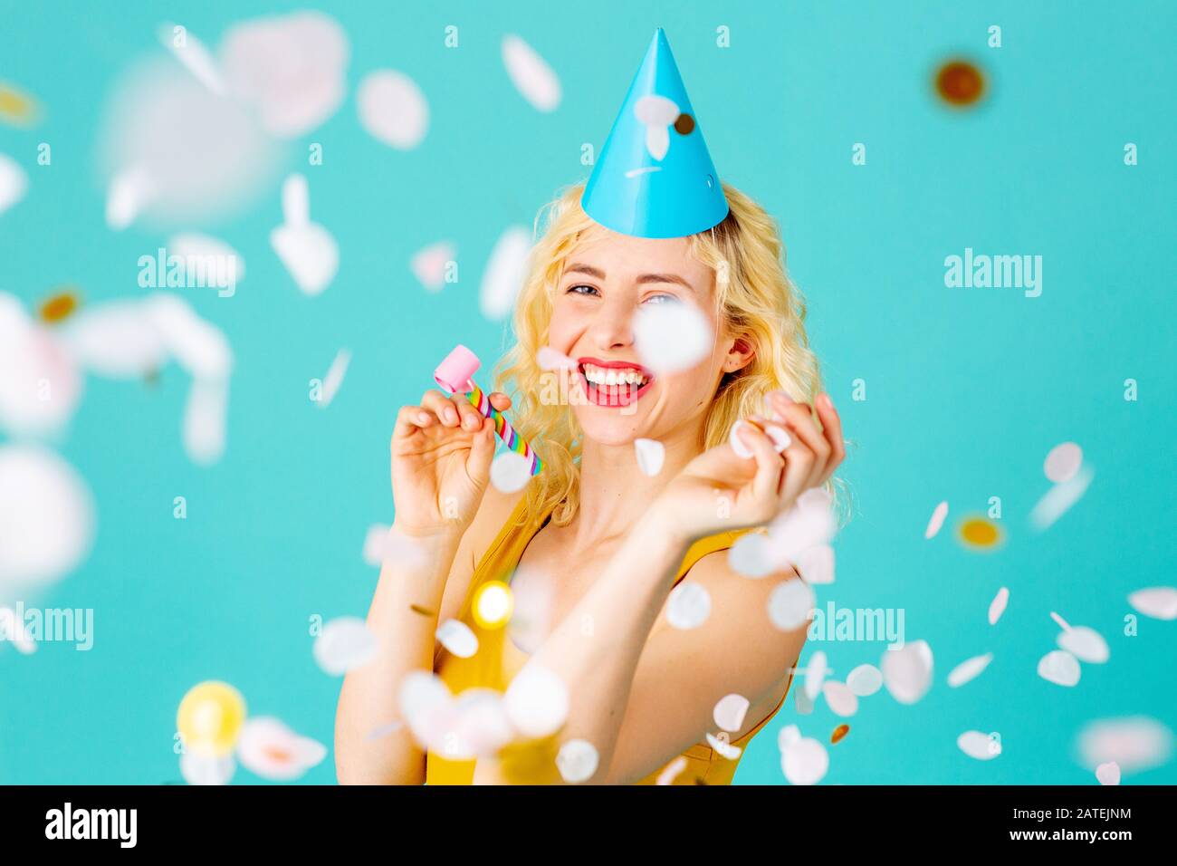 Portrait d'une jeune femme heureuse et souriante célébrant son anniversaire amusant avec chapeau de fête et confetti tombant, isolée sur bleu Banque D'Images