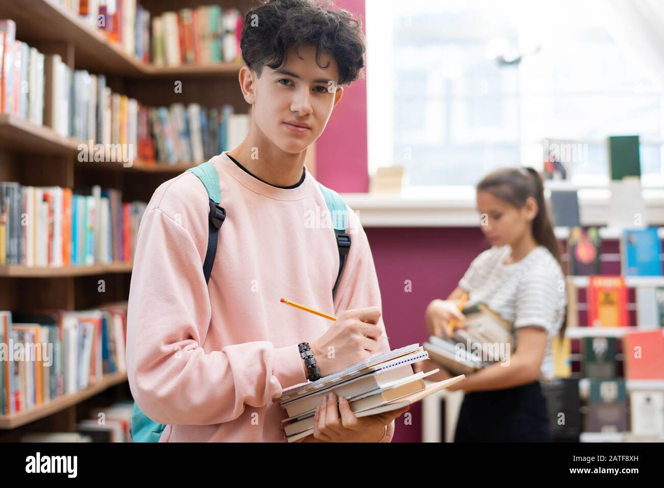 Un adolescent intelligent en sweat-shirt qui vous regarde tout en vous tenant à la bibliothèque Banque D'Images