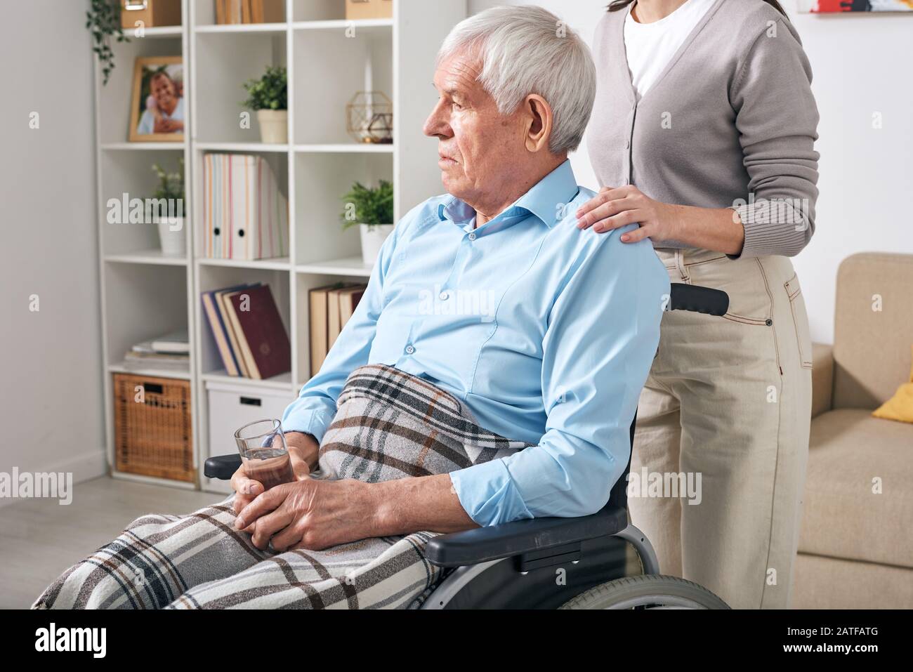 Homme handicapé âgé avec un verre d'eau assis sur le fauteuil roulant Banque D'Images