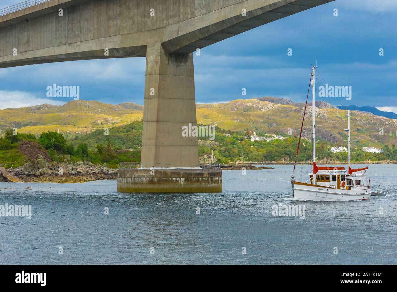 Pont de l'île de Skye avec bateau de croisière blanc et rouge passant sous le célèbre pont. Montagnes et cottages en arrière-plan. Paysage. Banque D'Images