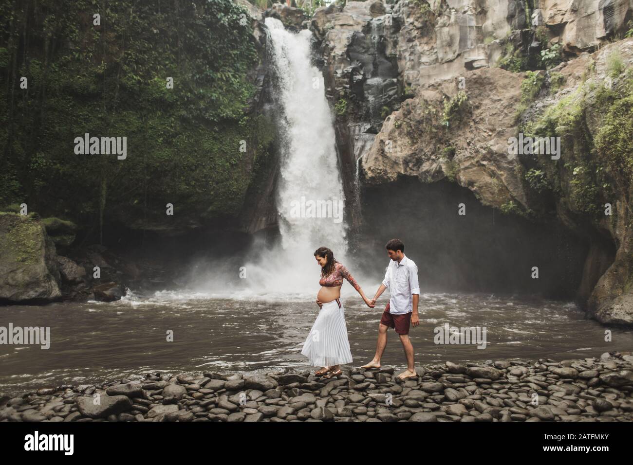 Young pregnant couple dans l'amour avec la vue étonnante de Tegenungan cascade cascade. La lumière du soleil du matin, heureux ensemble, la grossesse billet de vie. Banque D'Images