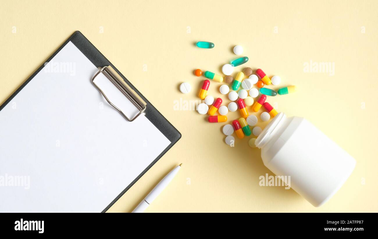 Presse-papiers médicaux et capsules colorées débordant de la bouteille blanche sur fond jaune. Plat, vue du dessus. Concept de pharmacie et de médecine Banque D'Images