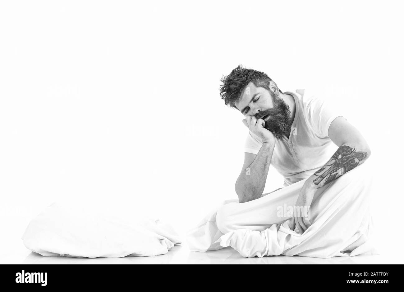 Homme épuisé, a besoin de se détendre, de repos, de sieste, de l'espace de copie. Homme bearded endormi sur fond blanc. L'hipster avec barbe et moustache s'endormit tout en étant assis au lit. Endormez-vous. Banque D'Images