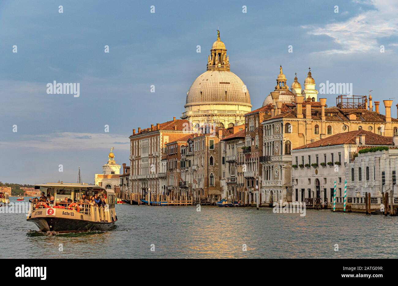 Un vaporetto ou un bateau-bus le font le long Du Grand Canal de Venise avec le dôme de la basilique Santa Maria della Salute en arrière-plan Banque D'Images