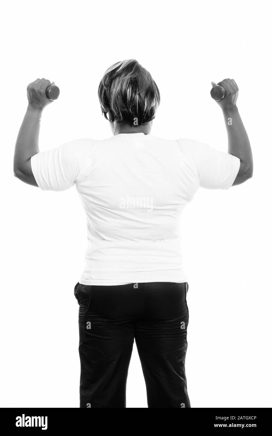 Vue arrière de la femme noire grasse africaine avec les deux haltères levés prêts pour la salle de gym Banque D'Images