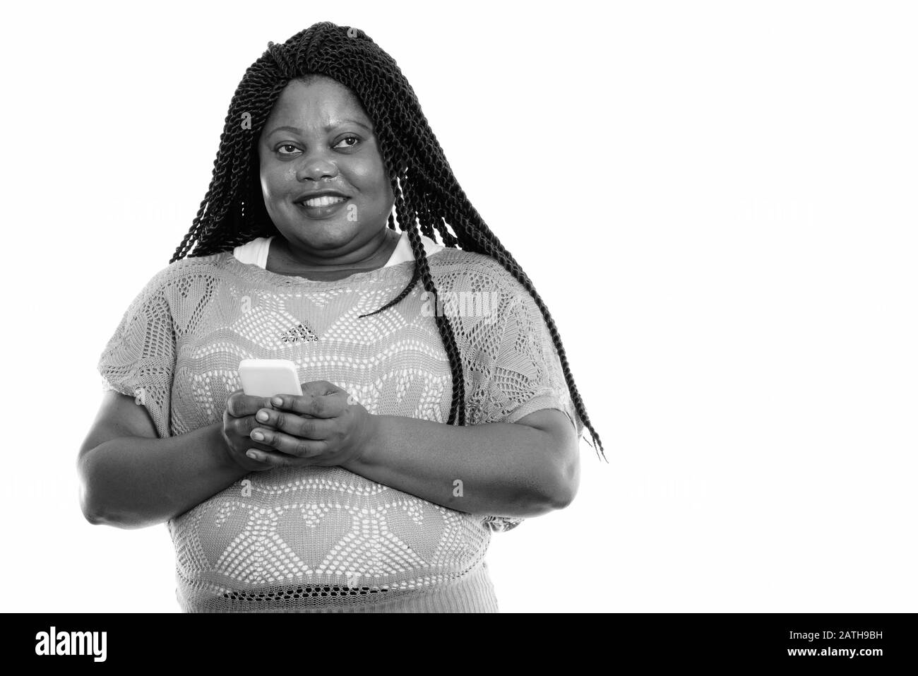 Studio tourné d'une femme africaine noire heureuse souriant et pensant tout en tenant le téléphone mobile Banque D'Images