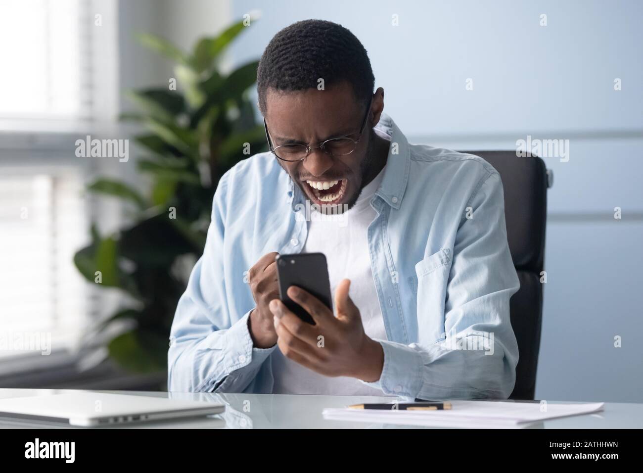 Un homme africain qui tient un téléphone portable se sent indigné d'avoir des problèmes de gadgets Banque D'Images