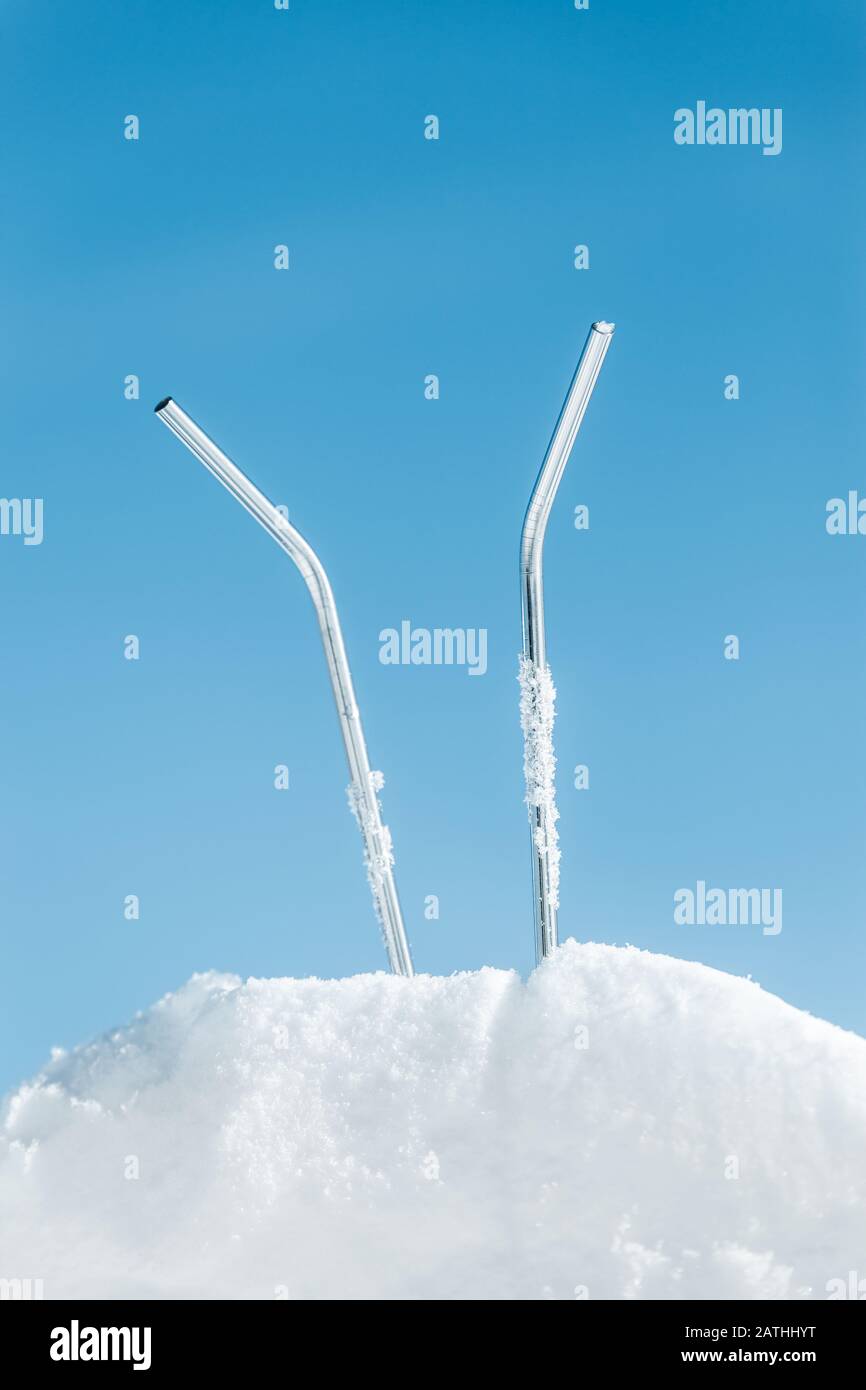 Pailles à boire métalliques durables dans la neige glacée, fond bleu ciel avec copyspace, boissons concept et cocktails Banque D'Images
