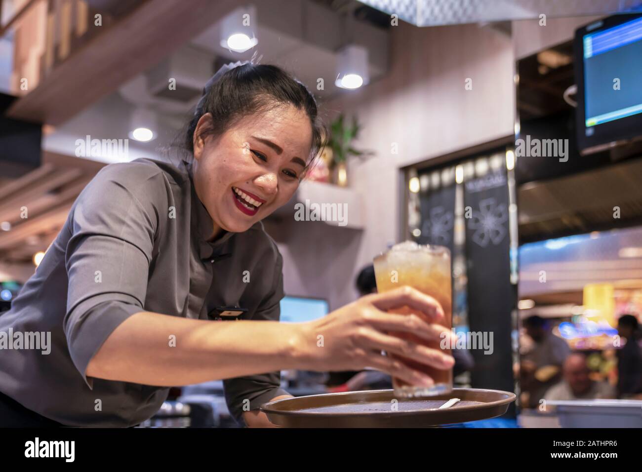 Thaïlande, Phuket, Patong. 3 janvier 2020 : une serveuse souriante sert un verre avec un cocktail et un jus de fruits. Bonne atmosphère dénaturée, bonne Banque D'Images