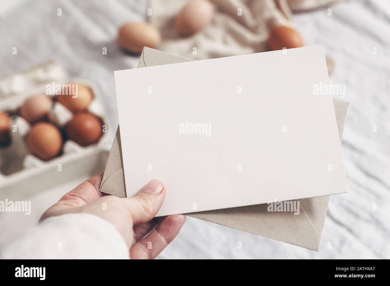 Gros plan de la main de la femme tenant une carte en papier vierge. Maquette de carte de vœux. Motif printemps, Pâques. Photo de stock féminine. Arrière-plan flou Banque D'Images