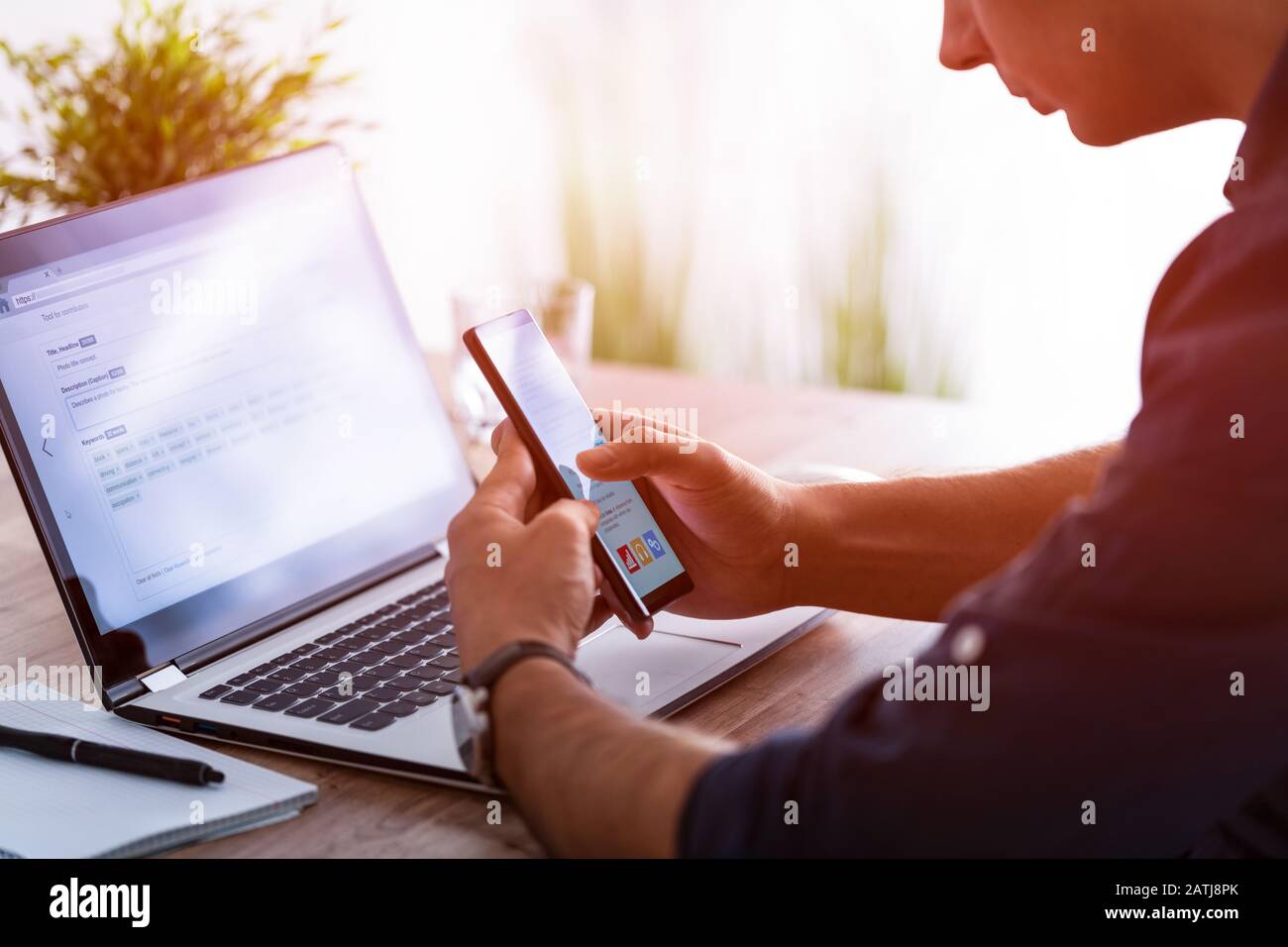 L'homme travaille à la maison et utilise un smartphone et un ordinateur portable. Silhouette d'un homme occupé. Une main tient et utilise le téléphone, l'autre écrit dessus Banque D'Images