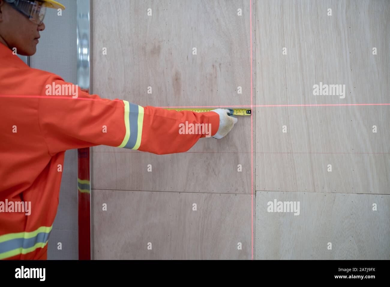 Carpenter utilise une bande de mesure pour mesurer la zone au niveau vertical à l'aide d'une machine laser. Banque D'Images