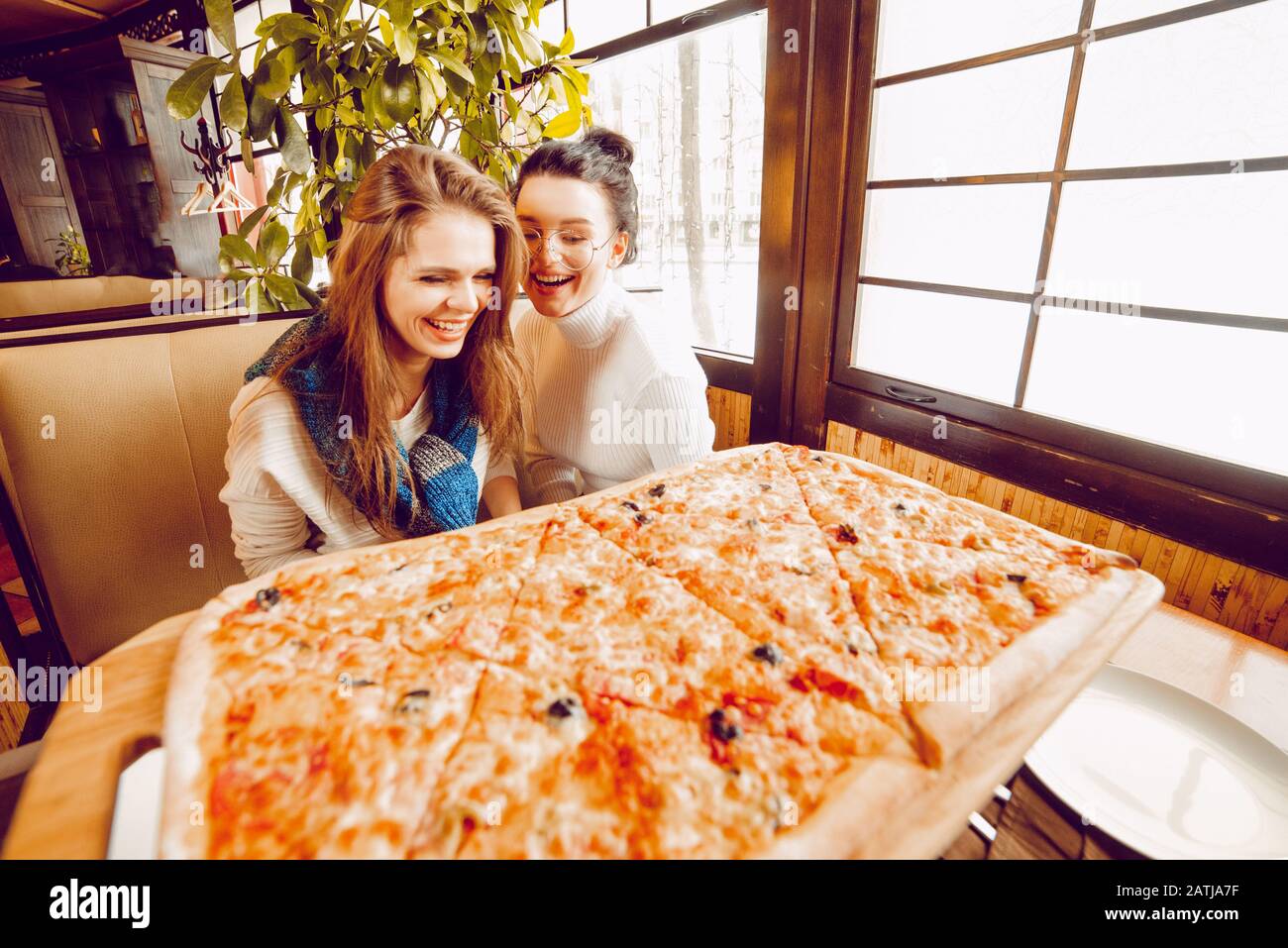 Filles dans une pizzeria avec une énorme pizza en tranches. Grande pizza sur la table. Amies dans un café Banque D'Images