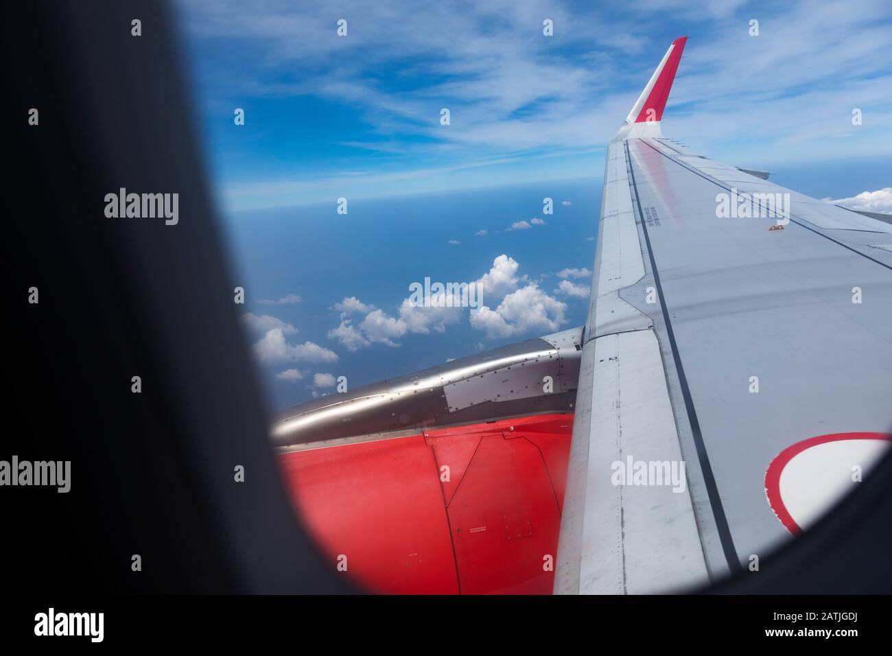 Vue depuis la fenêtre de l'avion Airbus A 320 lors d'une journée ensoleillée en regardant le long de l'aile avec des badgements d'entreprise rouges, un ciel ensoleillé et des nuages Banque D'Images