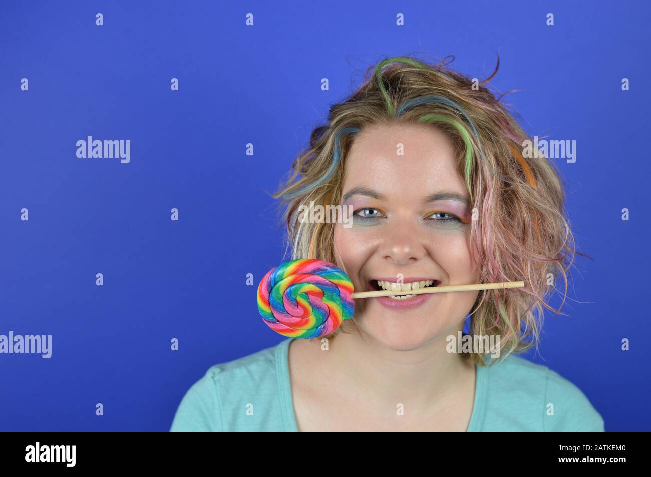 portrait d'une jeune femme blonde avec des cheveux colorés et une grande sucettes entre ses dents s'amuser et regarder dans l'appareil photo Banque D'Images