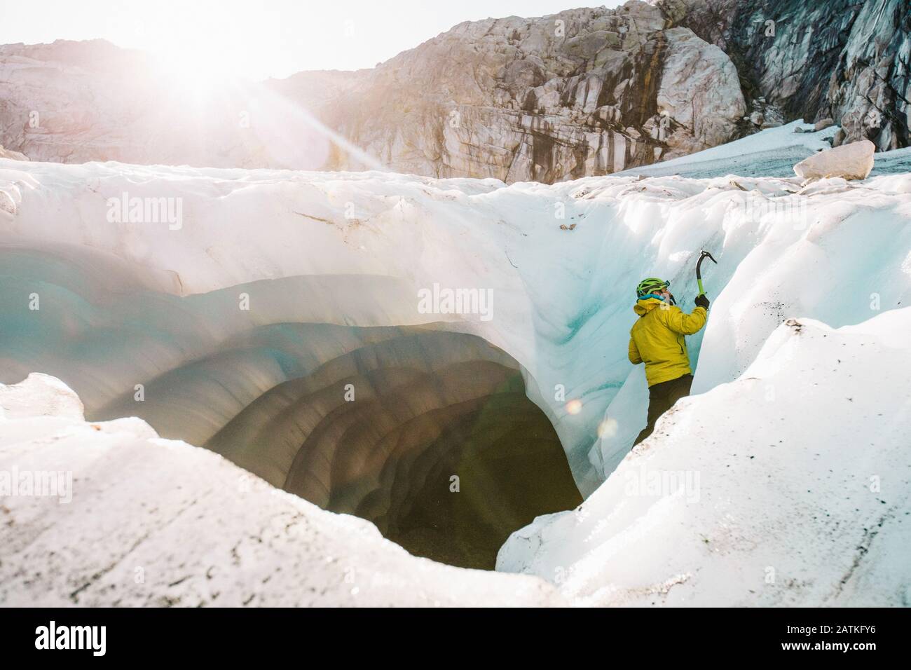Vue latérale de l'homme grimpant sur la glace à l'extérieur de la grotte glaciaire. Banque D'Images