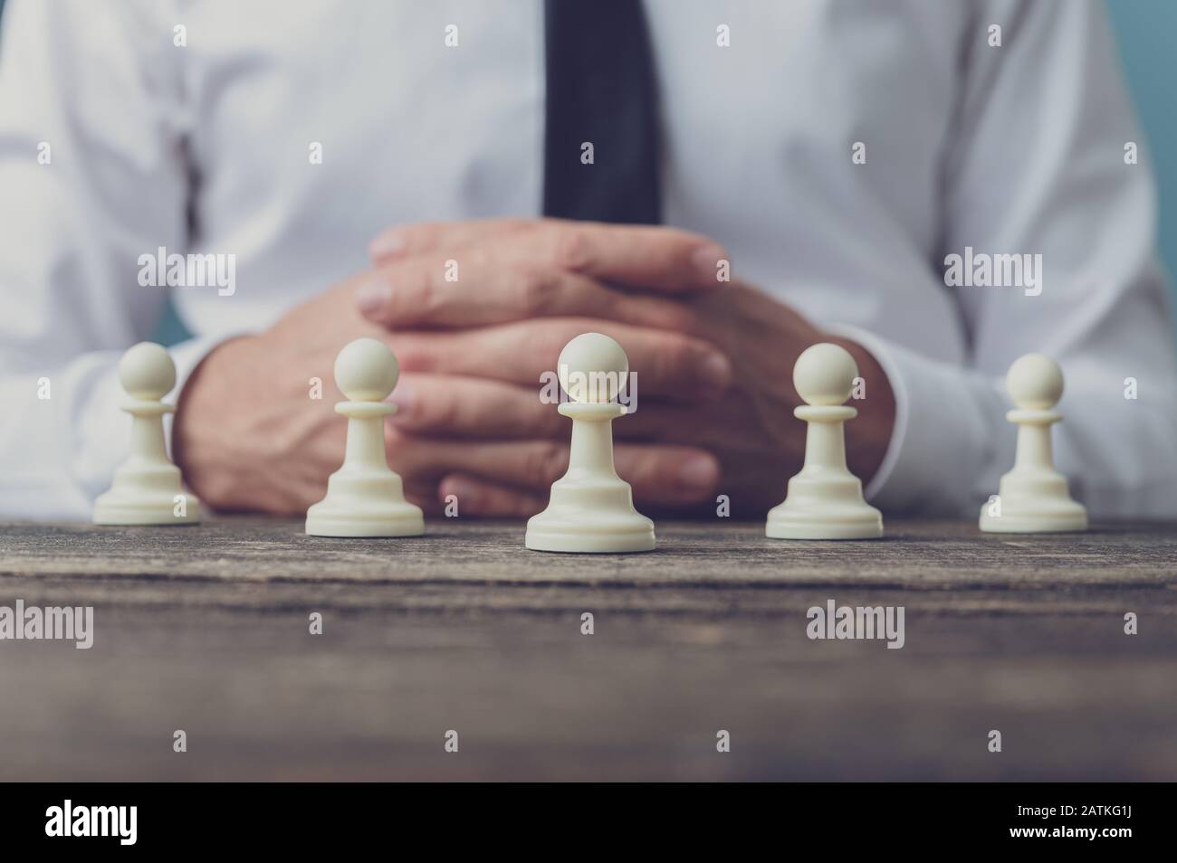 Homme d'affaires assis à son bureau avec cinq pièces d'échecs en pion positionnés devant lui. Image conceptuelle de l'emploi et du leadership. Banque D'Images