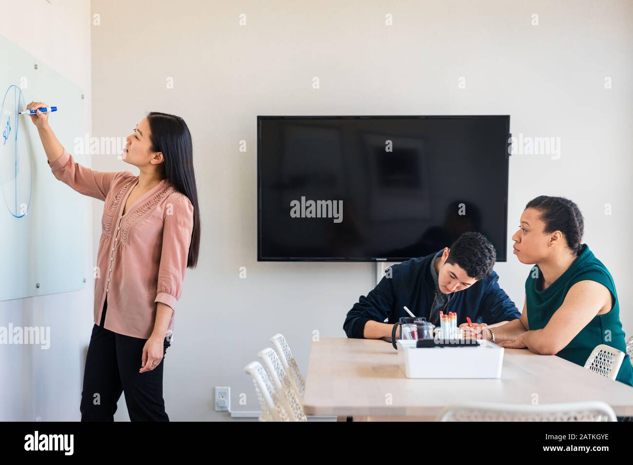 femme d'affaires dessinant diagramme sur tableau blanc tout en planifiant avec des collègues en réunion au bureau Banque D'Images