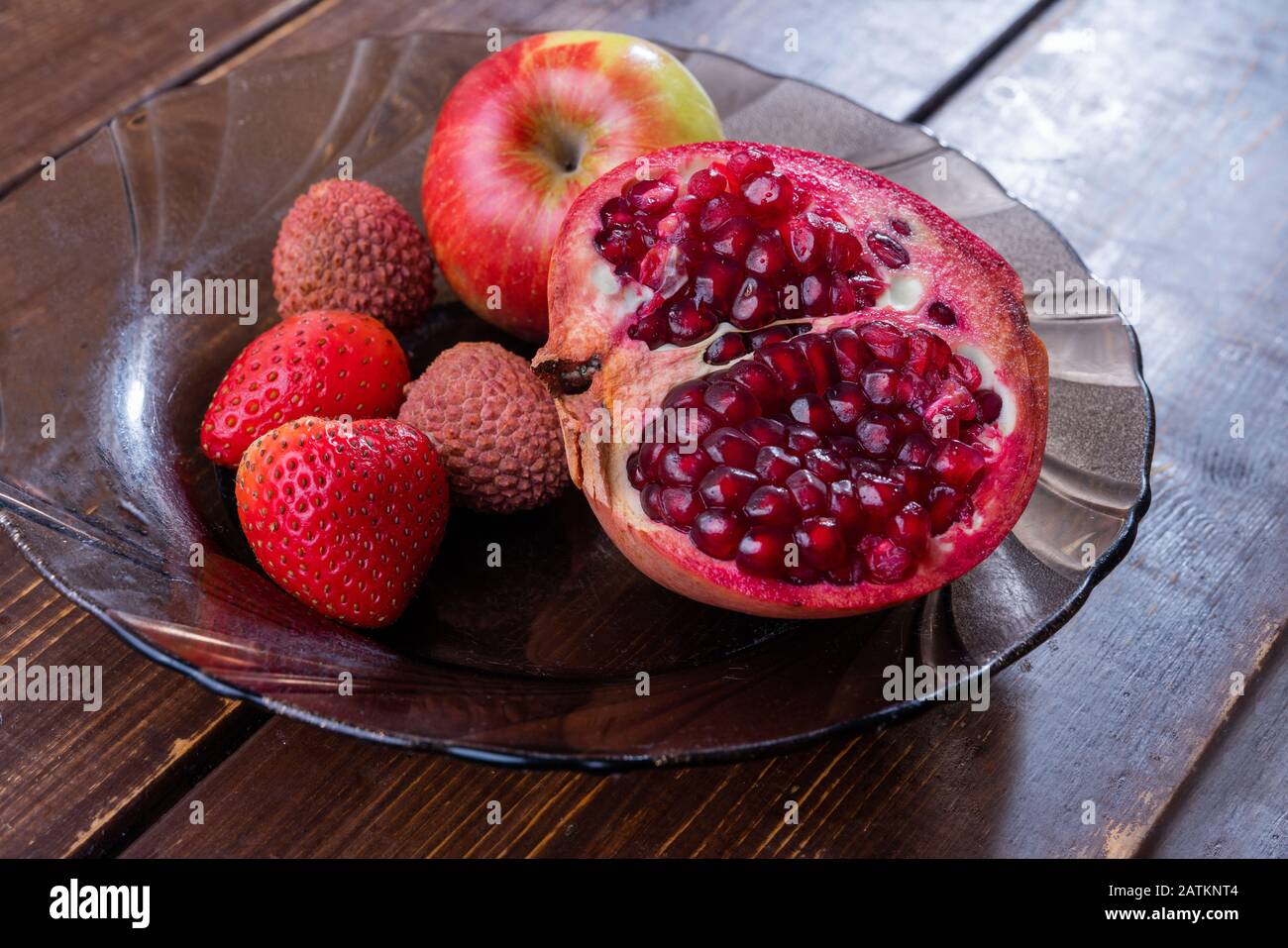 Fruits sur plaque : grenade, fraise à pomme et lychee sur table en bois brun Banque D'Images