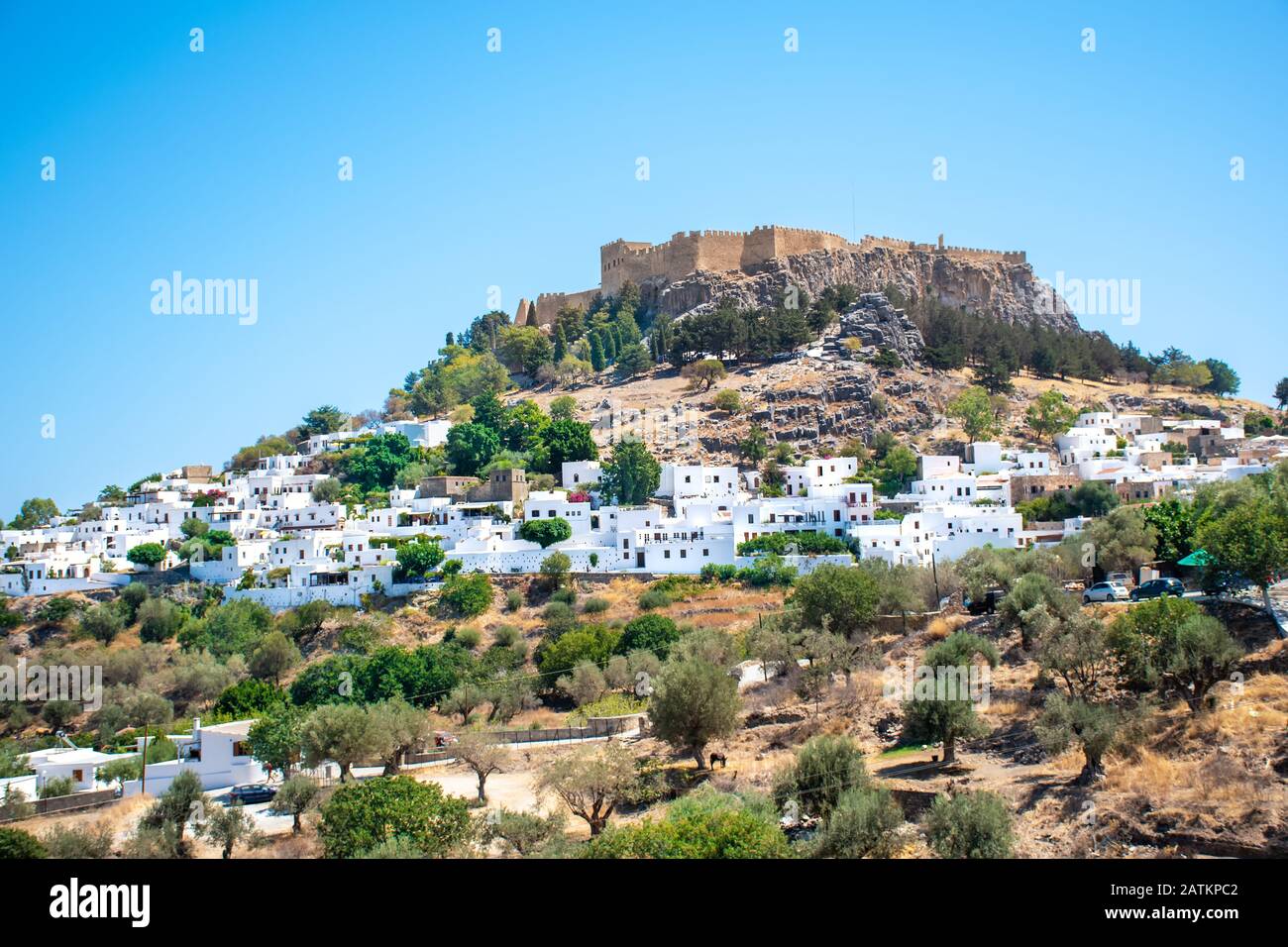 Vue sur les maisons blanches du village de Lindos parmi les arbres avec Acropole en arrière-plan (Rhodes, Grèce) Banque D'Images