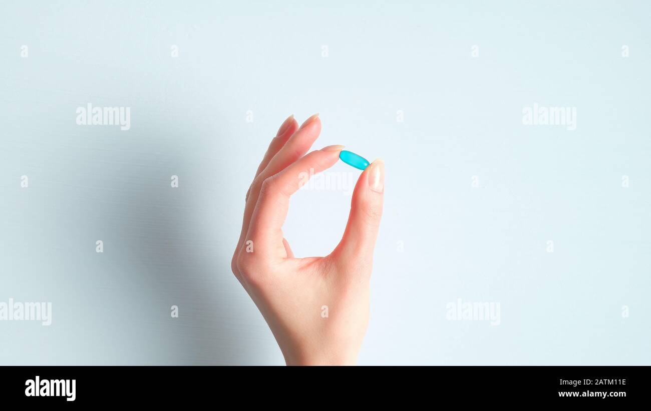 Main féminine tenant la capsule de la pilule médicale sur fond bleu. Concept de pharmacie et de médecine Banque D'Images