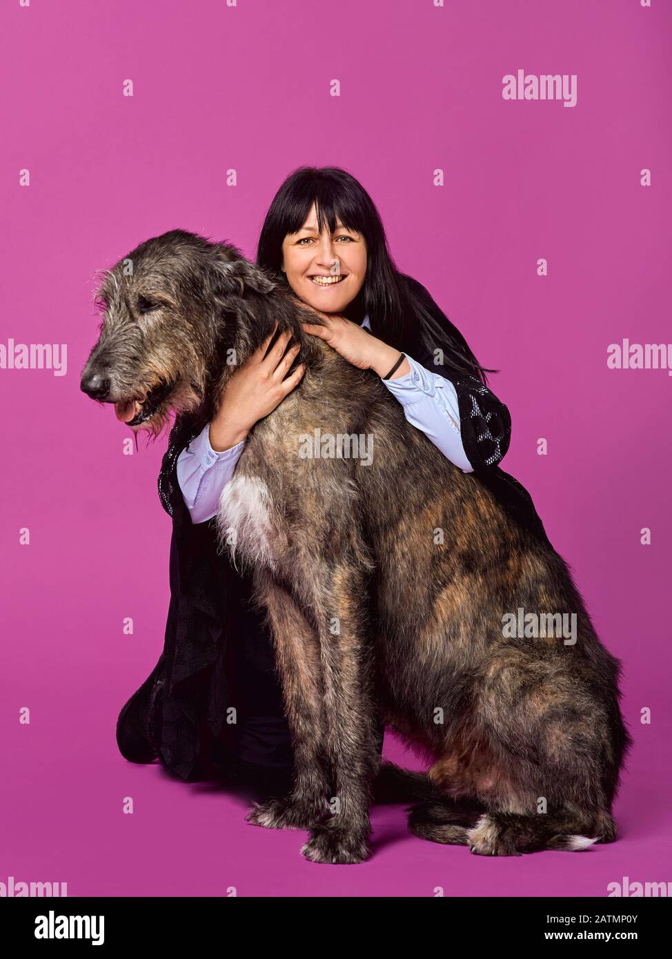 Femme souriante et joyeuse brunette avec Wolfhounds irlandais gris sur fond de couleur fuchsia en studio photo. Concept d'amitié, d'amour, d'animaux de compagnie. Banque D'Images